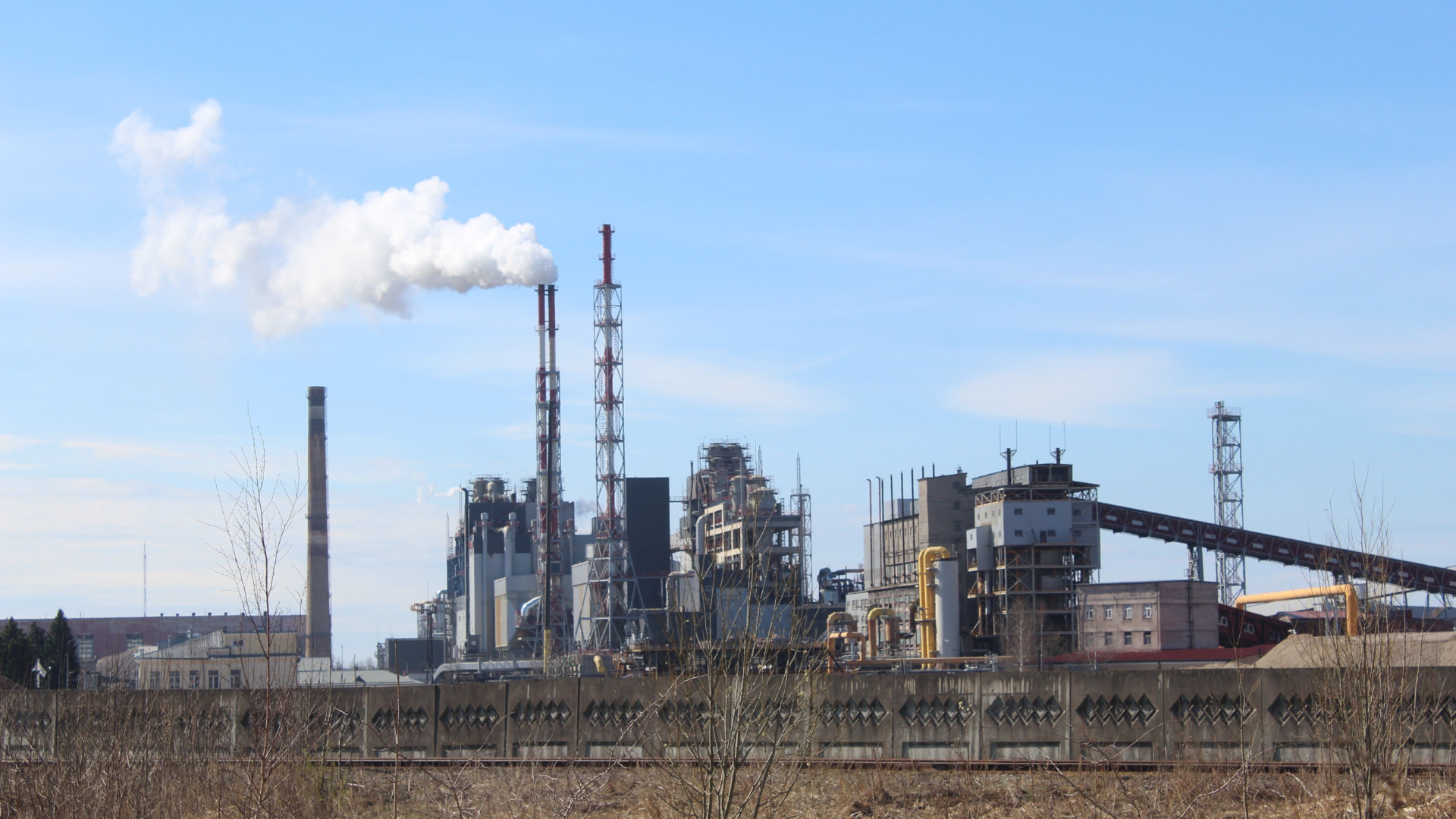 Planta industrial con chimeneas emitiendo humo junto a la vía férrea